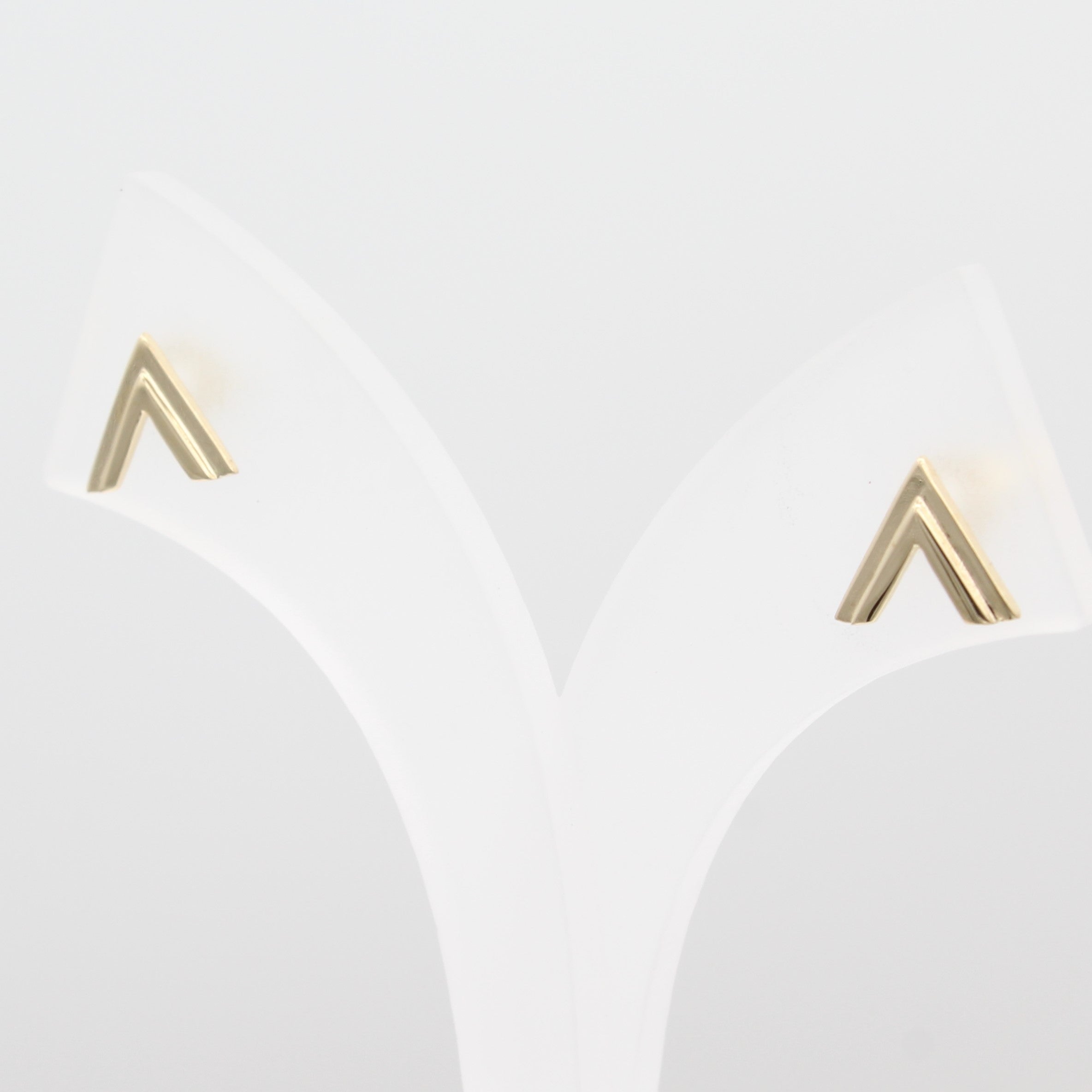 A close-up view of 14k Yellow Gold Double Chevron Earrings on a white jewelry display.