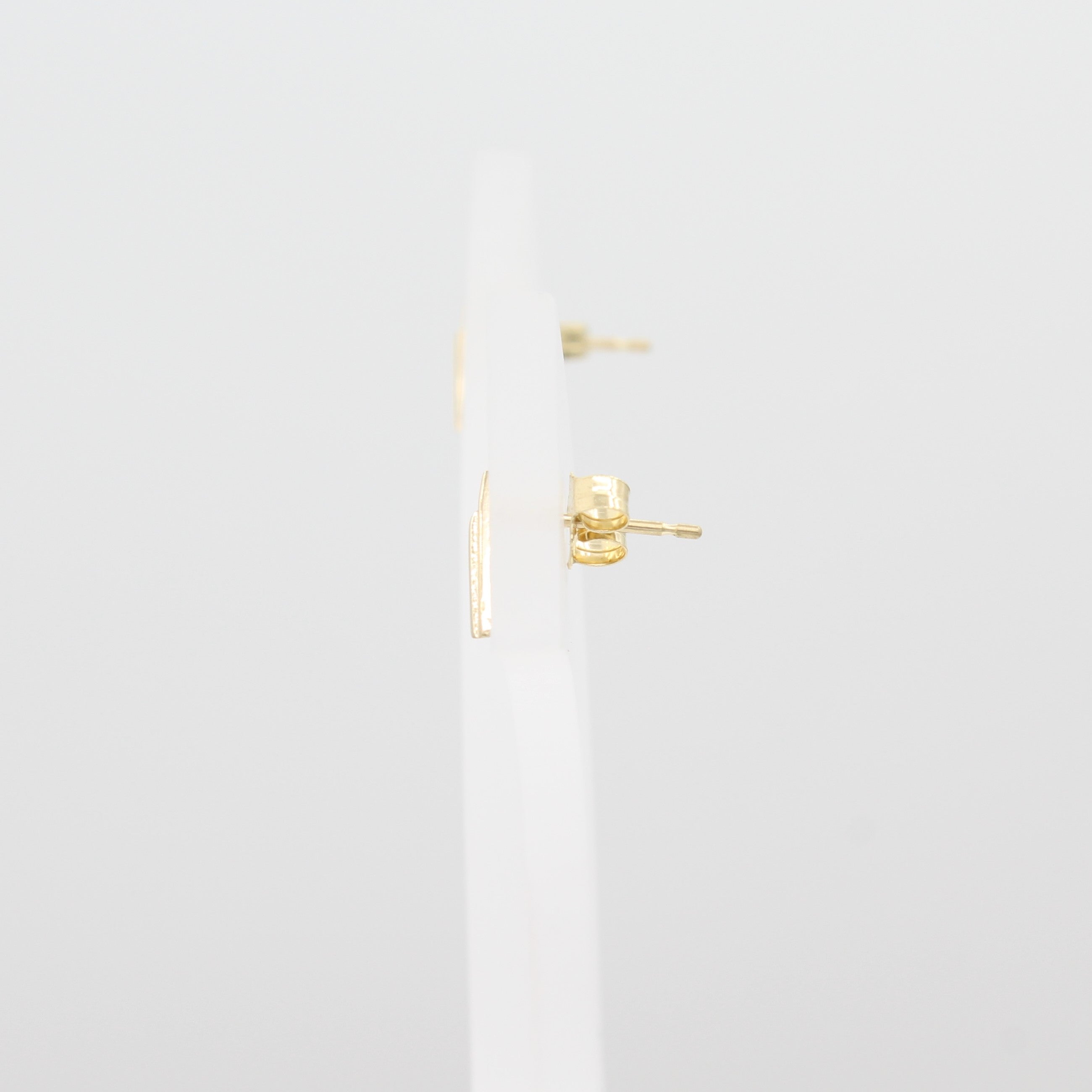 A close-up side view from the right of 14k Yellow Gold Double Chevron Earrings on a white jewelry display with a peak of the earring backs. 