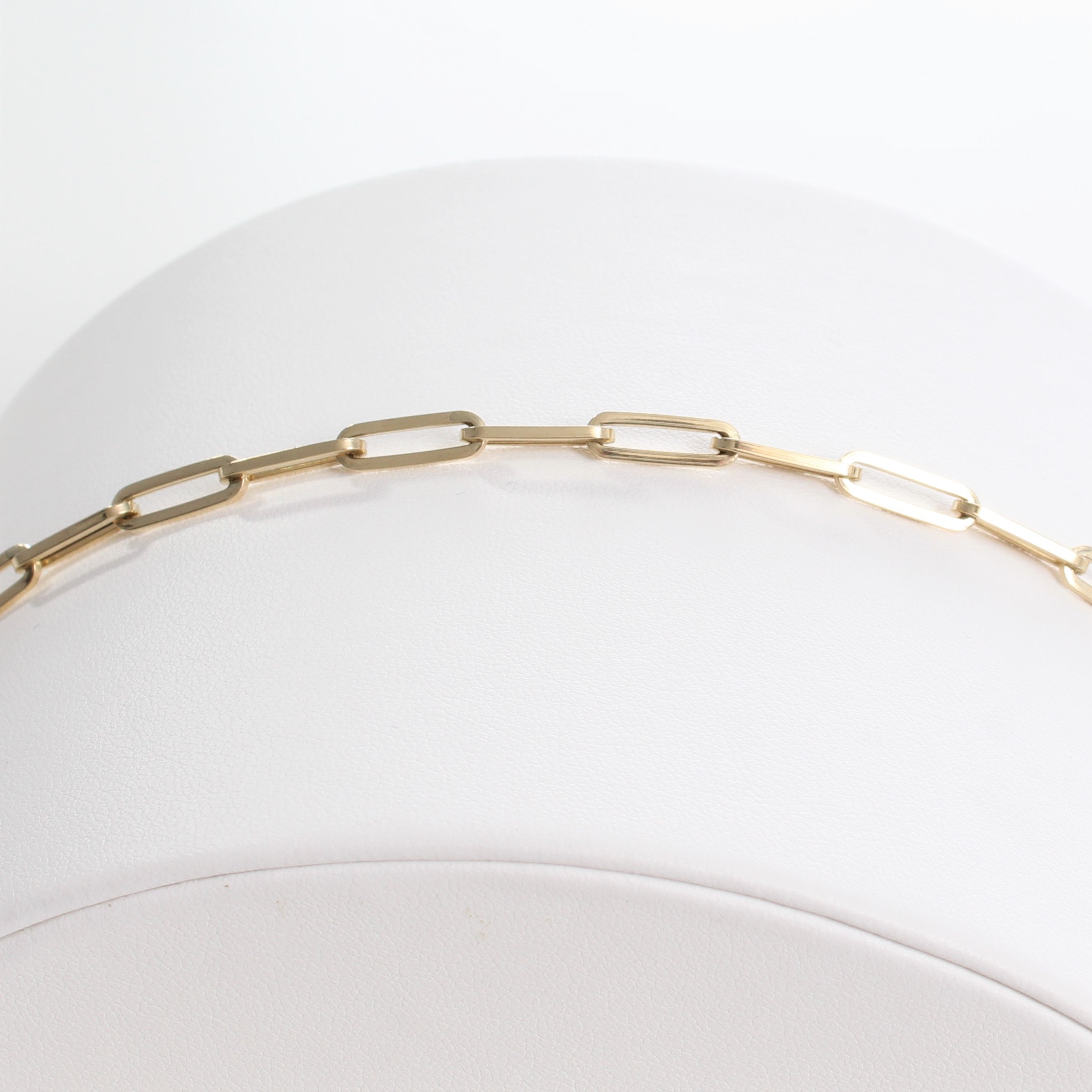14k Yellow Gold Retro Elongated Link Paperclip Medium Link Bracelet. close-up view of unclasped bracelet laid out on a white jewelry display.